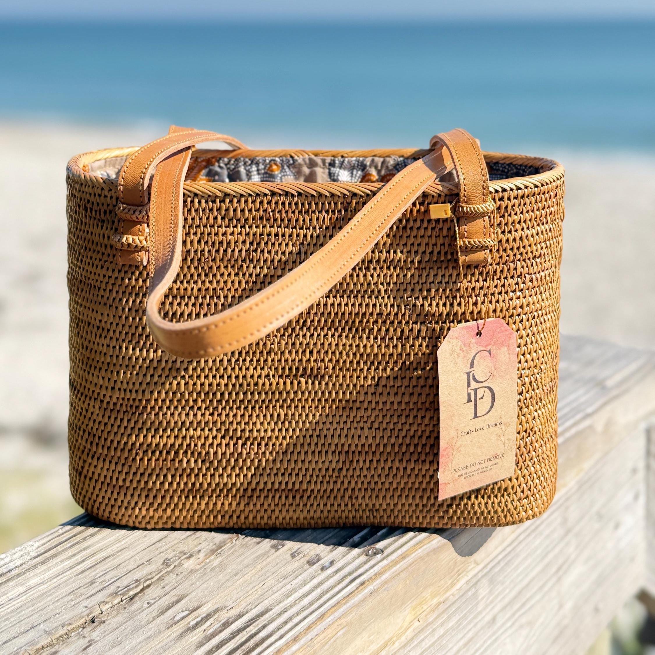 A woven straw handbag with a tag attached, placed on a wooden surface near the ocean.