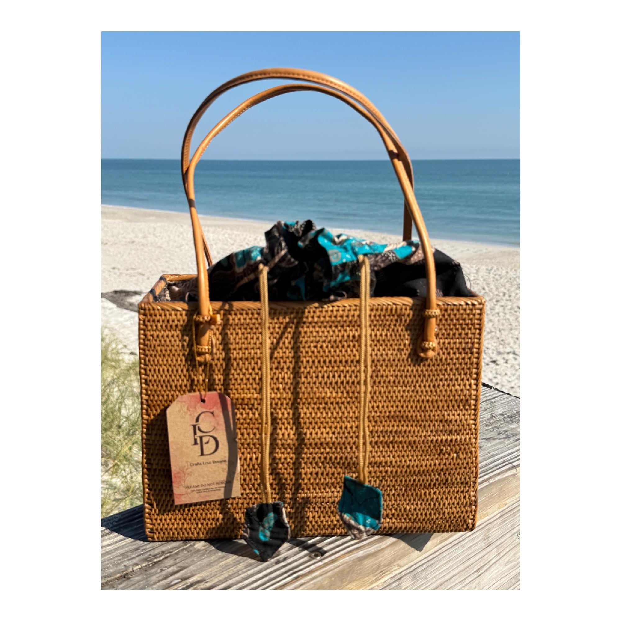Handwoven Bali rattan square tote with leather handles and batik drawstring liner on the beach from Crafts Love Dreams