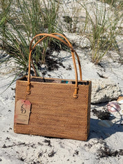 Handwoven rattan square tote with leather handles standing in the sand dunes
