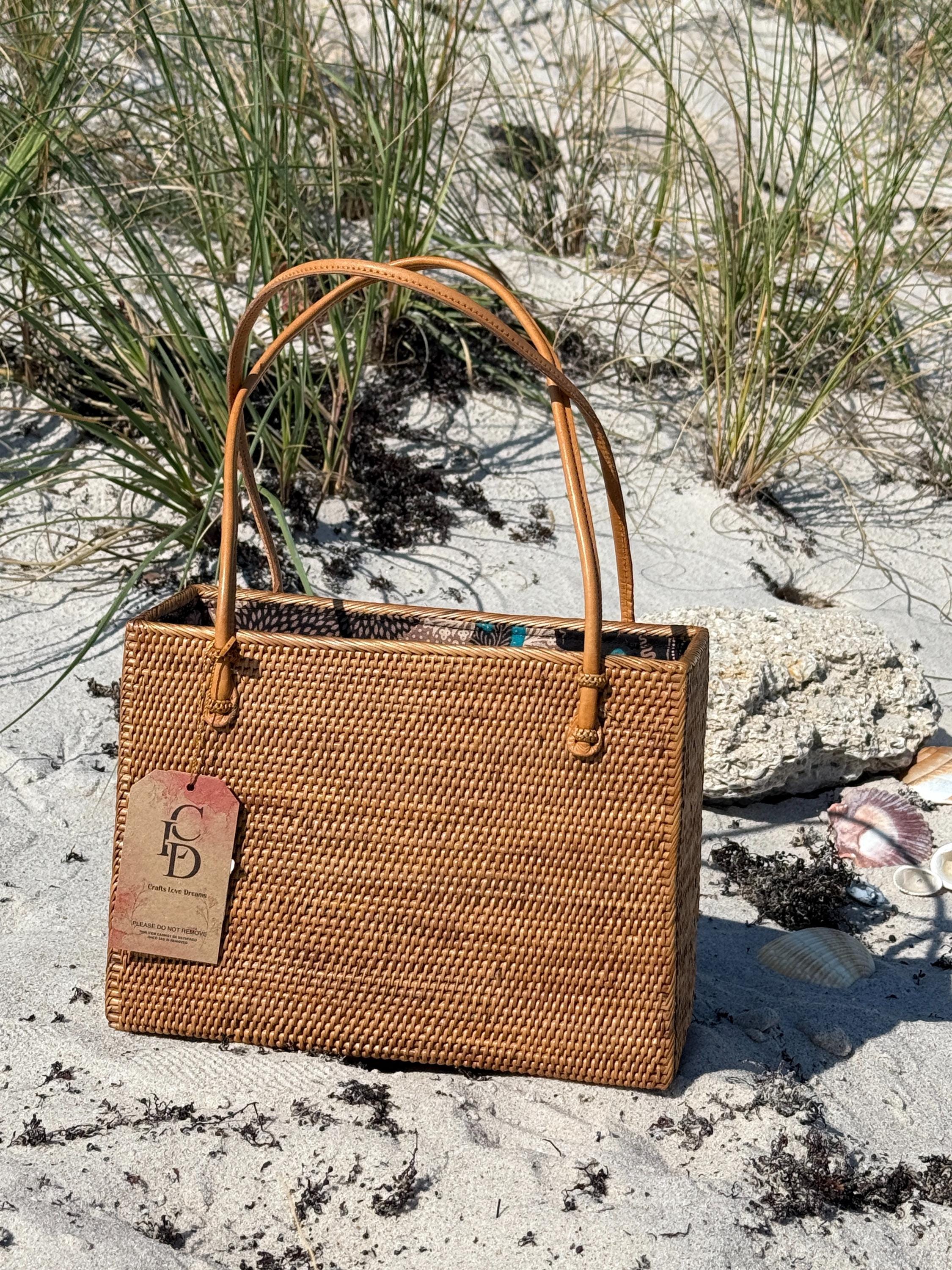 Handwoven rattan square tote with leather handles standing in the sand dunes
