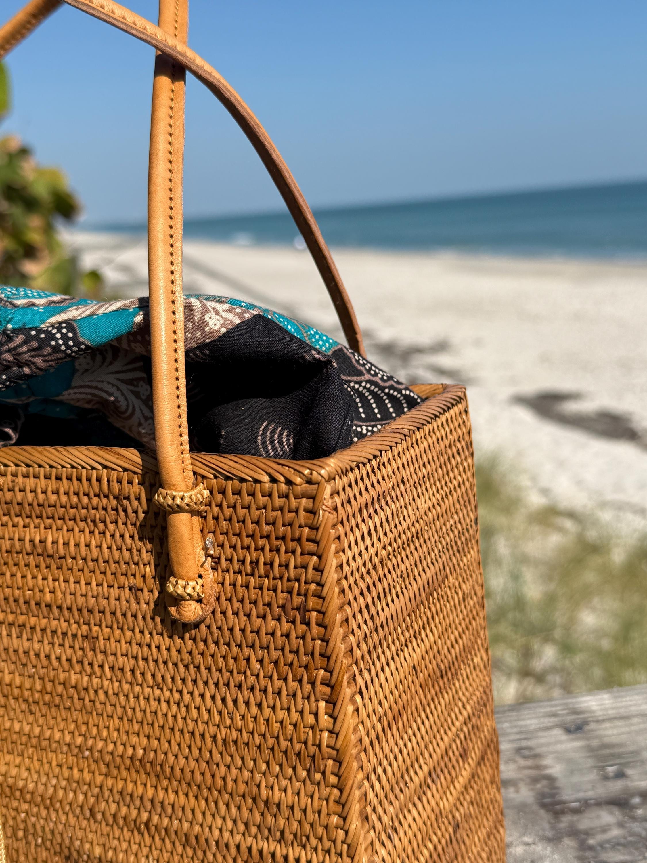 Close-up of the rattan square tote's leather handles and batik drawstring liner at the beach