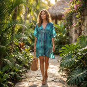 A woman in a blue and white striped dress walks down a path surrounded by lush greenery and tropical plants.