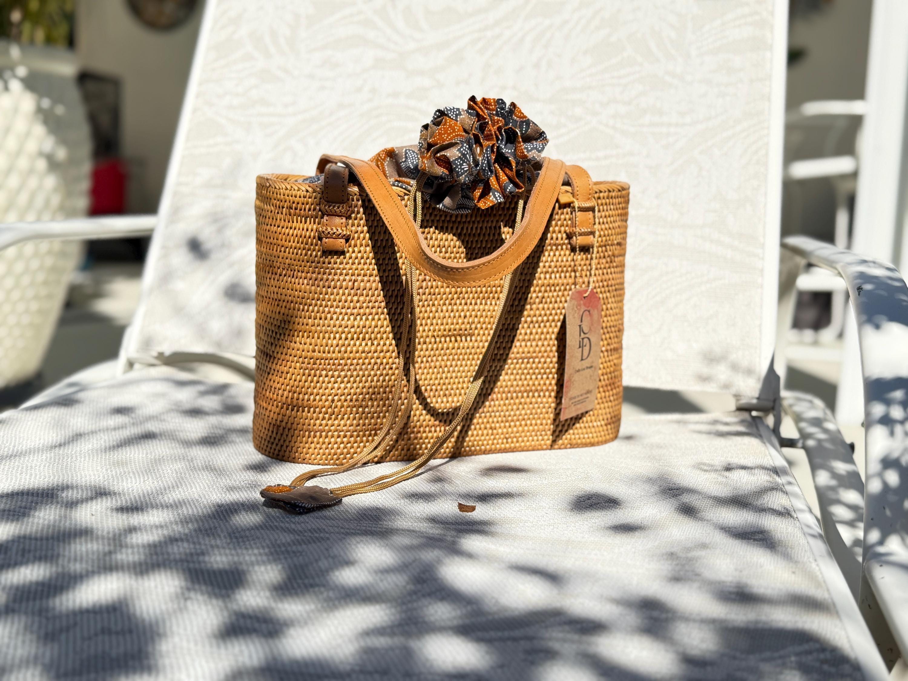 A woven straw handbag with a colorful scarf tied around the handle, placed on a white chair.