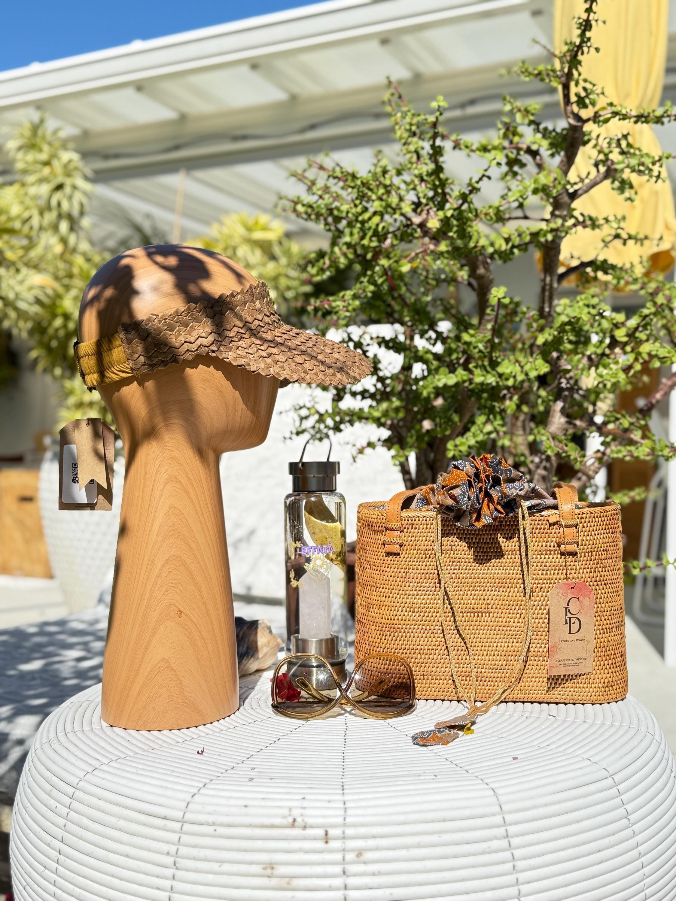 a variety of items, including a hat, sunglasses, a woven bag, and a bottle, arranged on a white table.