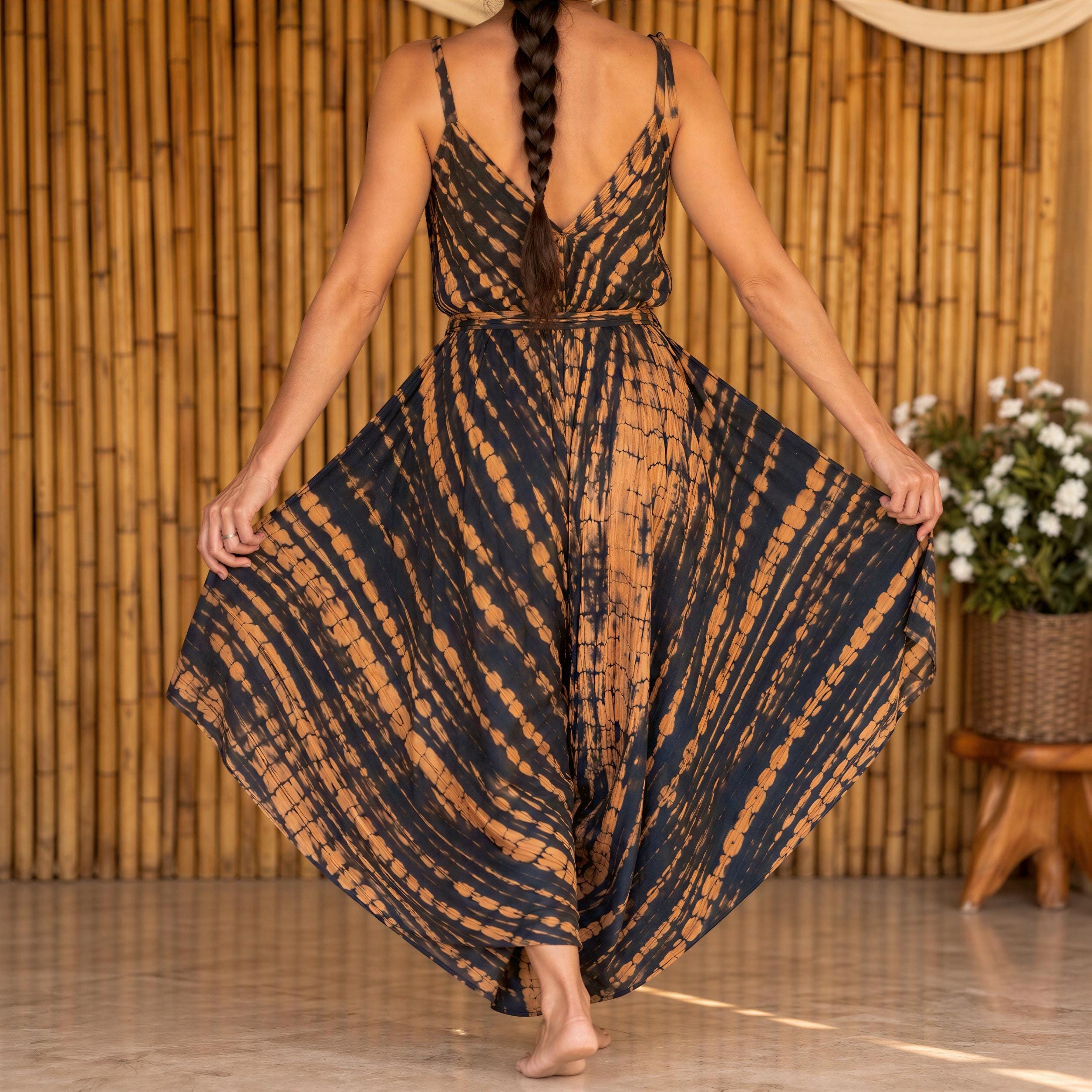 A woman wearing a long, tie-dye dress with a high neckline and a wide skirt, standing in front of a bamboo wall.
