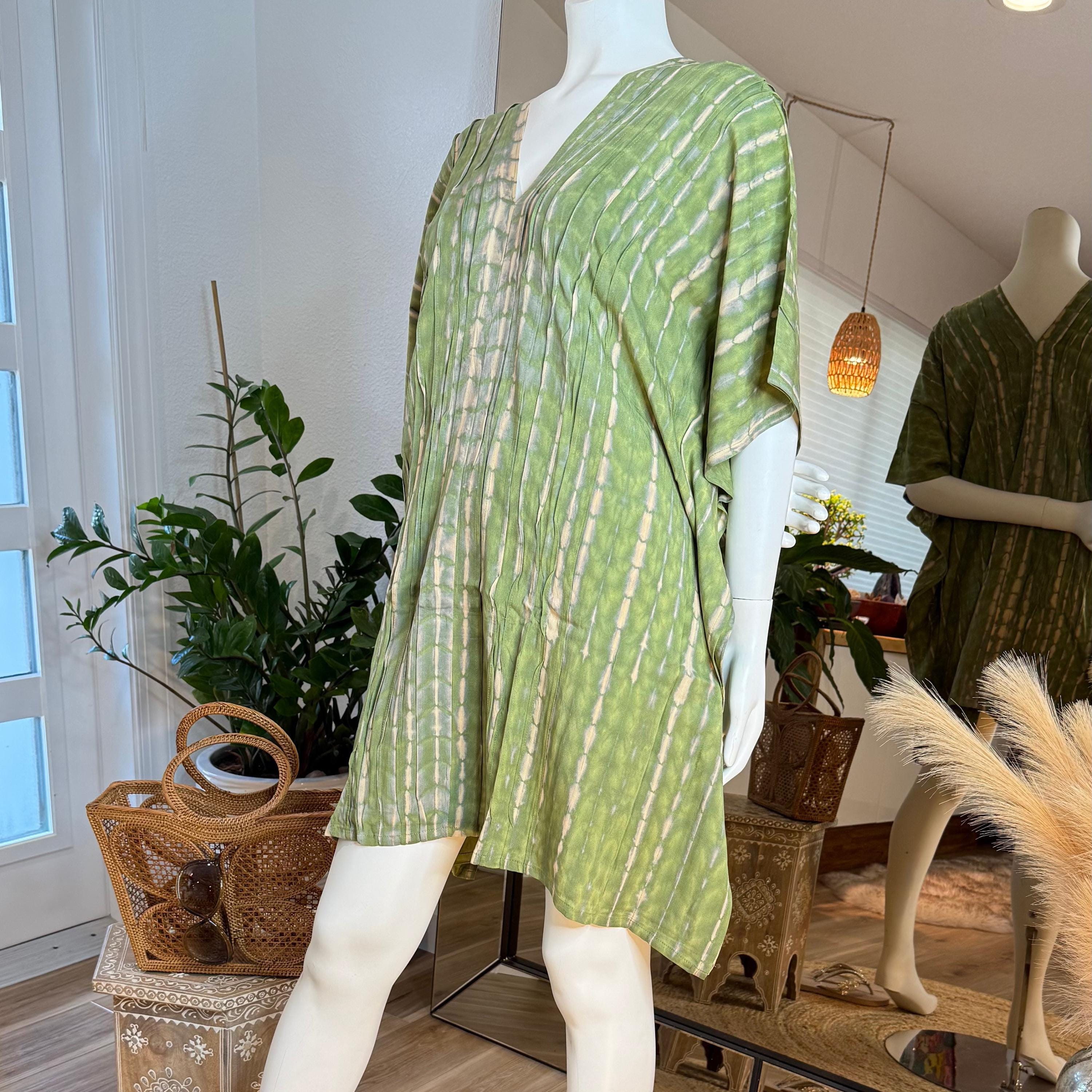 A mannequin wearing a green and white tie-dye dress stands in a clothing store, surrounded by potted plants and other decorative items.