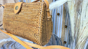 A woven straw purse with a metal clasp and strap is displayed in the image.