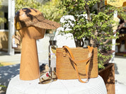 a wooden head with a straw hat, a woven straw bag, a pair of sunglasses, and a glass bottle on a white table.