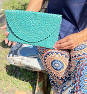 A person is sitting on a bench, holding a turquoise patterned handbag.