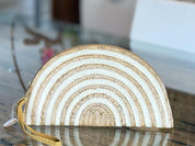 A white and beige woven purse with a curved shape and a handle, placed on a glass surface.