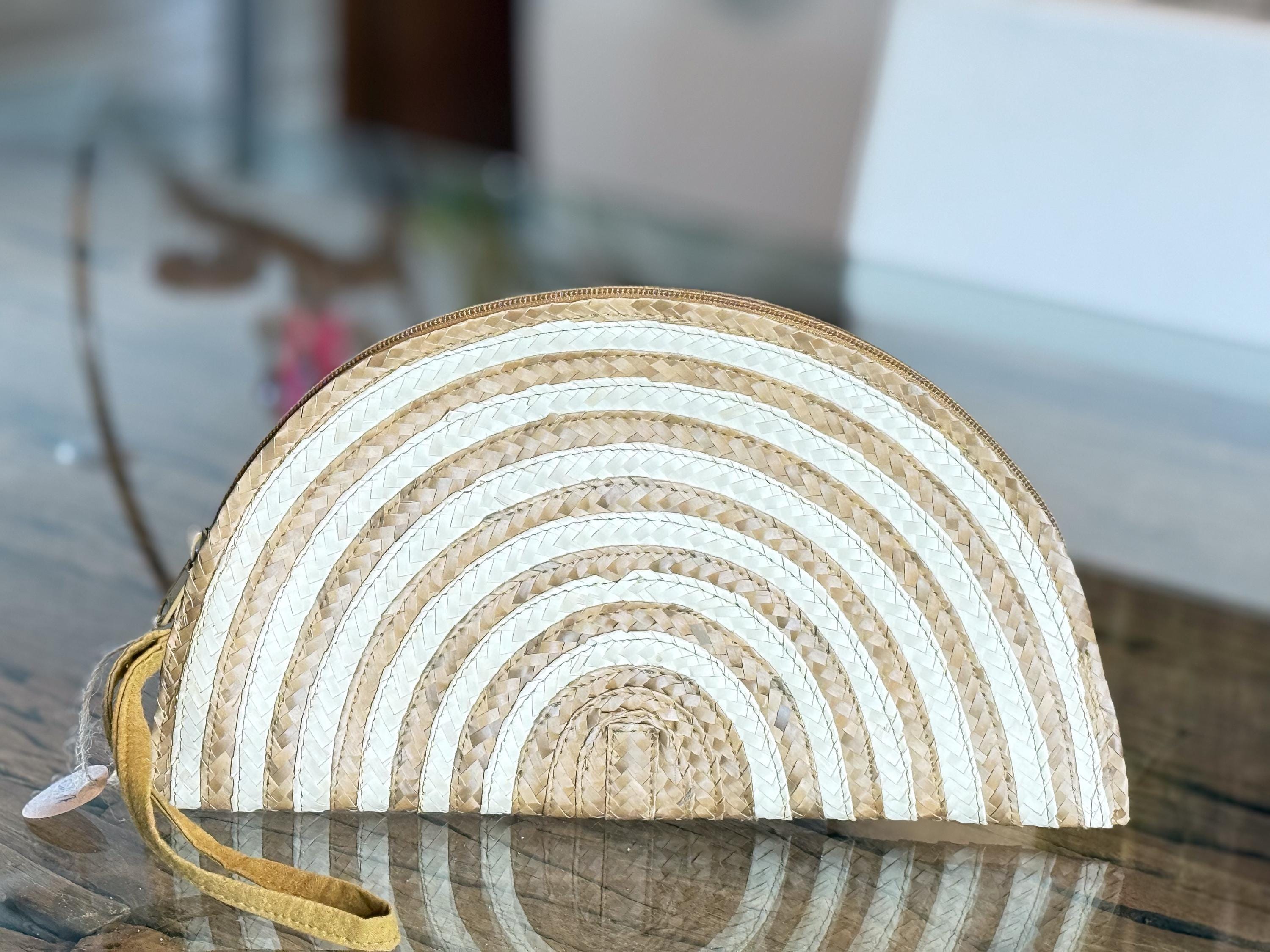 A white and beige woven purse with a curved shape and a handle, placed on a glass surface.