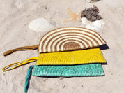 A stack of three colorful woven bags, including a striped purse and two yellow and green bags, rests on a sandy beach.