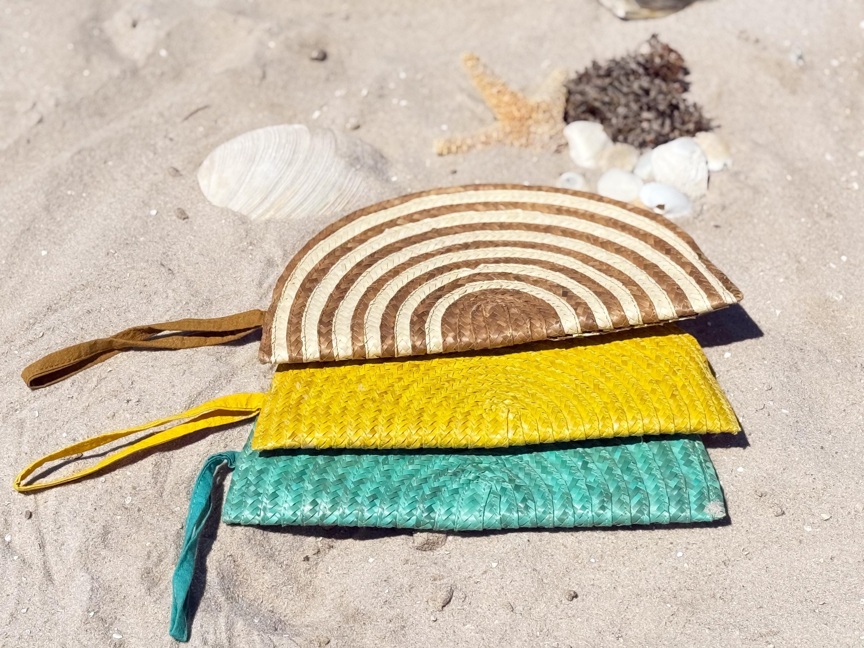 A stack of three colorful woven bags, including a striped purse and two yellow and green bags, rests on a sandy beach.