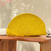 A bright yellow woven handbag is placed on a wooden surface, with a blurred background suggesting an outdoor setting.