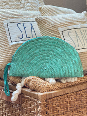 a wicker basket with a teal-colored purse resting on top of it, along with two beige pillows with the word "SEA" written on them.