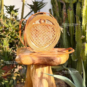 A round woven purse sits on a wooden stool in a lush, green garden setting.