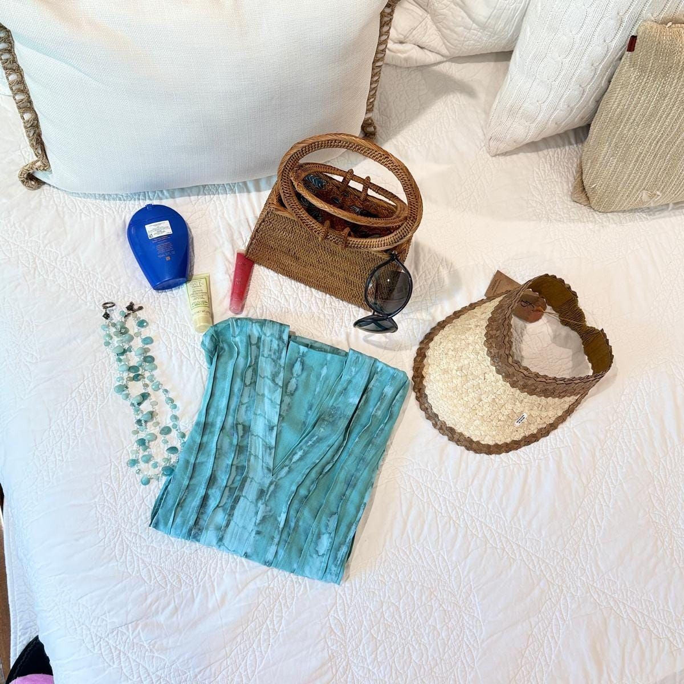 a variety of items laid out on a bed, including a blue bottle, a brown woven basket, a pair of sunglasses, a turquoise scarf, and a brown hat.