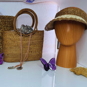 a woven handbag, a wooden headband, a purple butterfly figurine, and a small wooden object on a white surface.