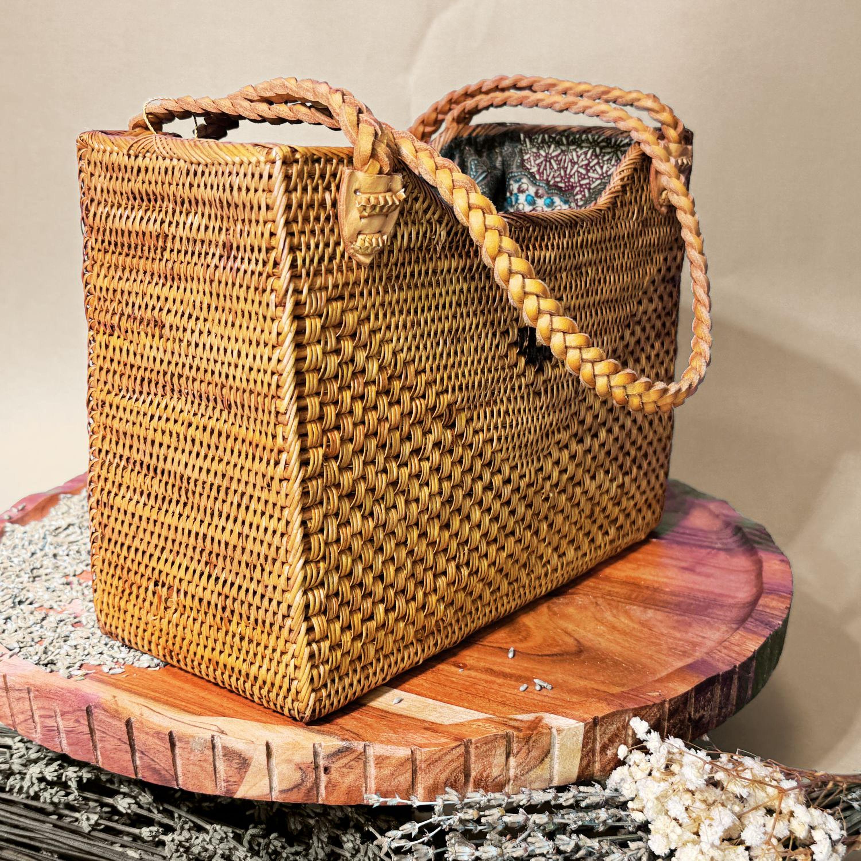 A woven straw bag with a braided handle, placed on a wooden surface.