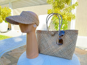 a hat stand with a hat and a handbag placed on it, set against a backdrop of greenery and a building.
