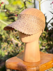A wooden mannequin head wearing a woven straw visor.