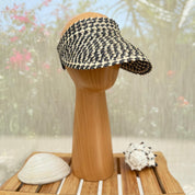 A black and white patterned visor is displayed on a wooden stand, accompanied by a seashell and a small white object.