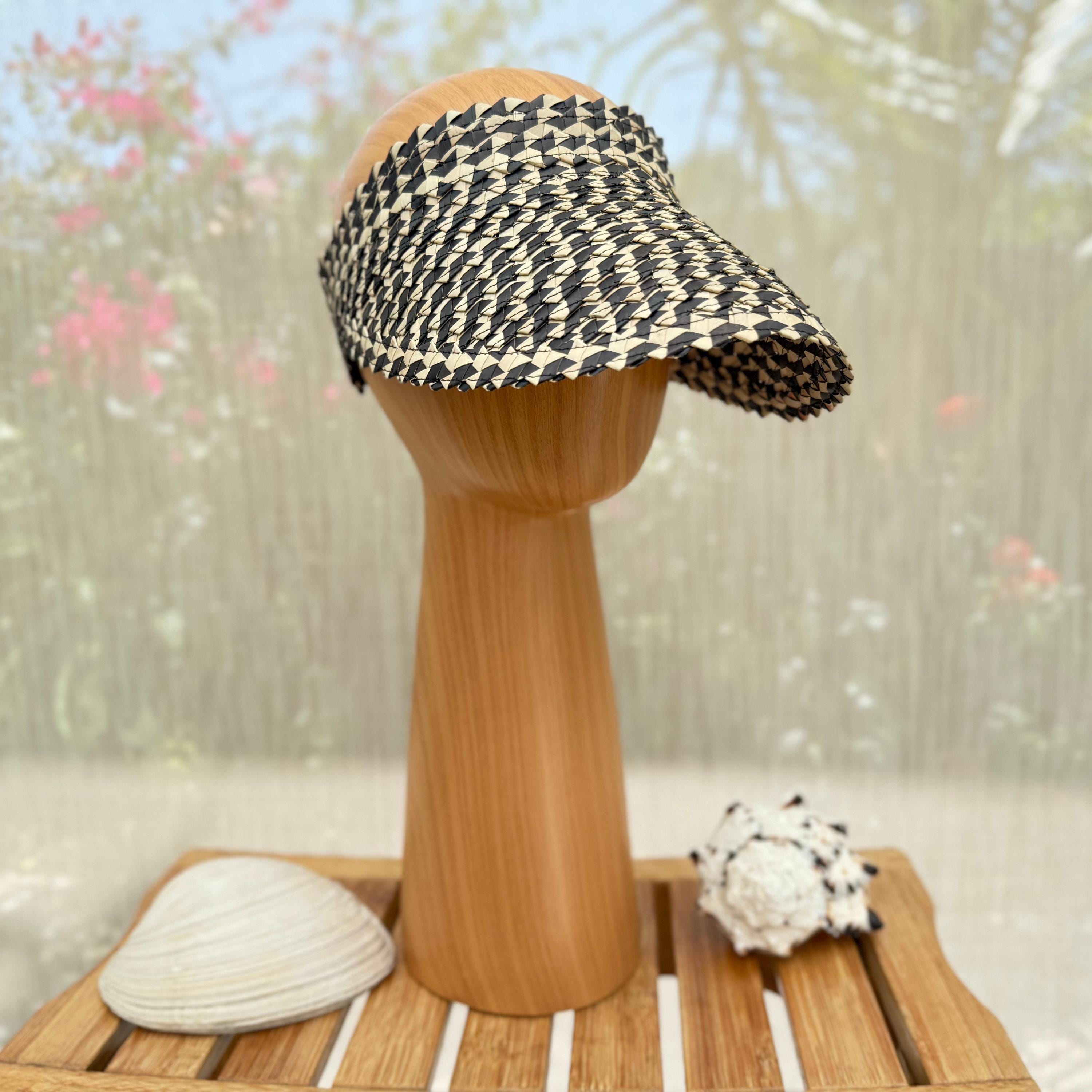 A black and white patterned visor is displayed on a wooden stand, accompanied by a seashell and a small white object.