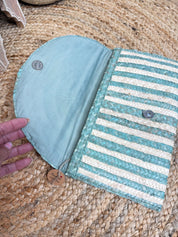 a hand holding an open, light blue and white striped purse or clutch bag.