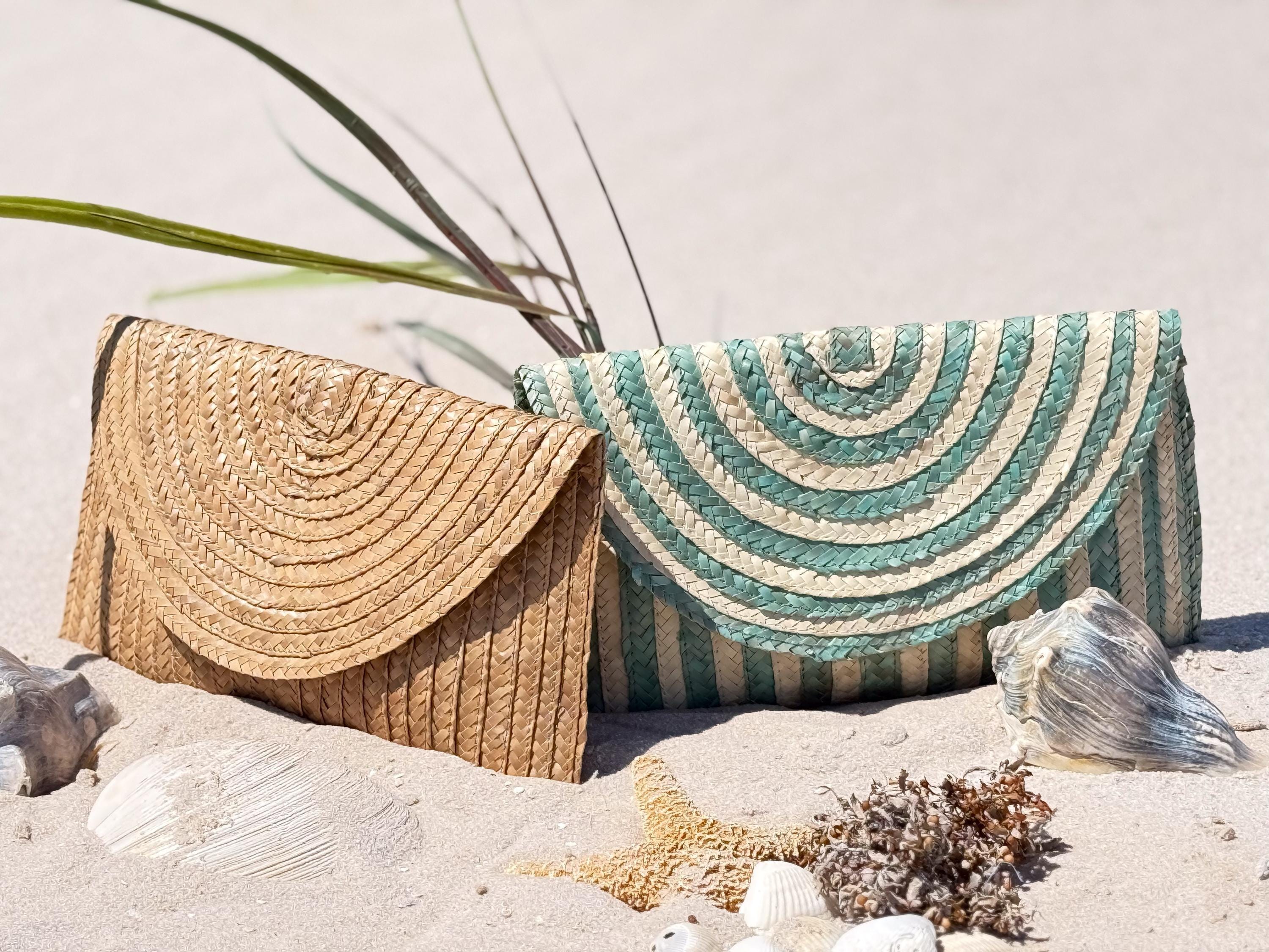 Two woven bags, one brown and one striped in blue and white, are placed on a sandy beach with seashells and a starfish nearby.