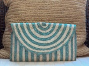 A striped clutch purse with blue and white stripes is placed on a woven pillow.