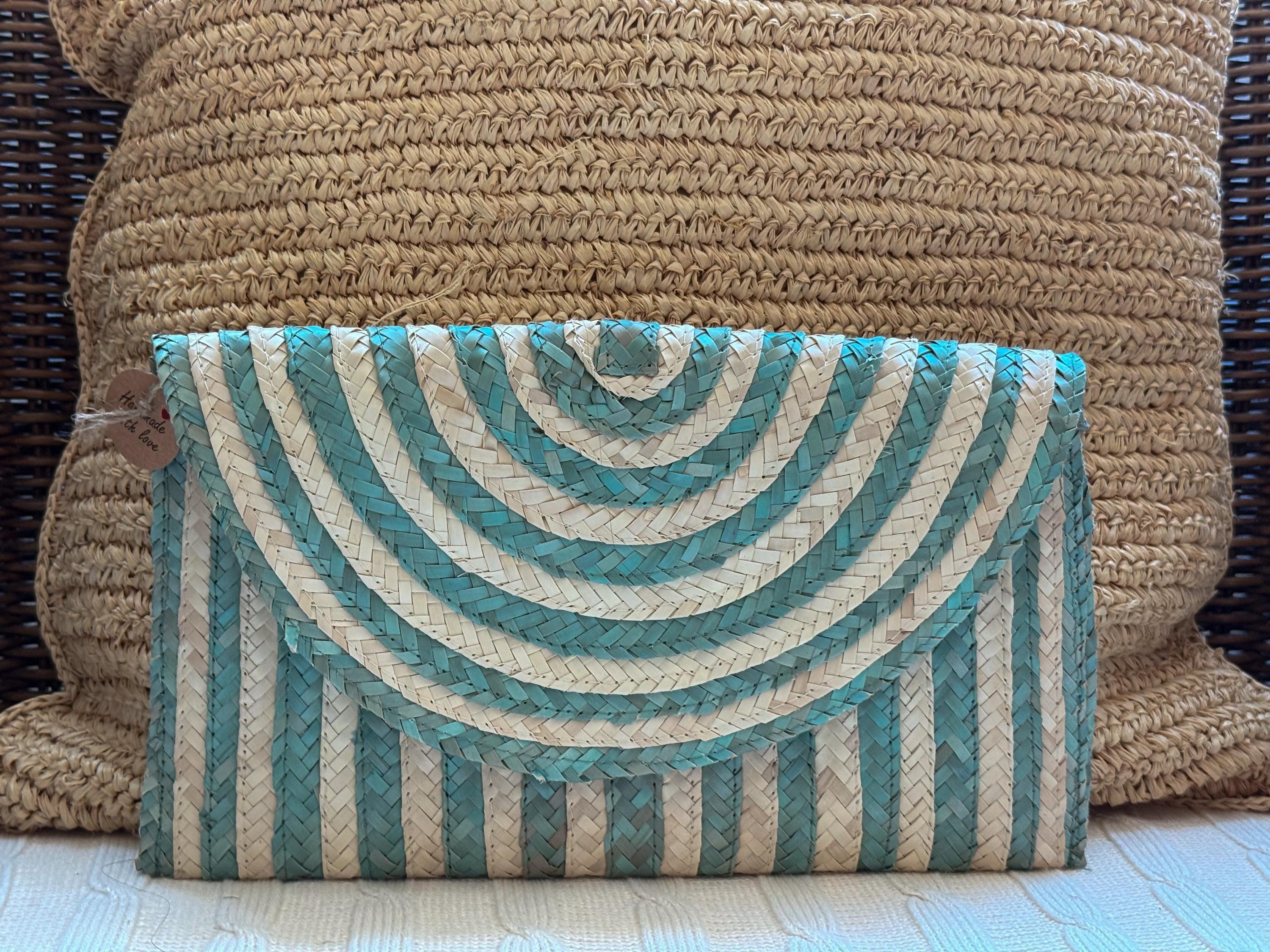 A striped clutch purse with blue and white stripes is placed on a woven pillow.