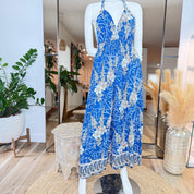 A mannequin wearing a blue floral jumpsuit with a halter neckline and a long skirt, displayed in a clothing store.