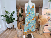 A mannequin wearing a blue and yellow floral print dress stands in a room with various decorative elements, including potted plants and a large mirror.