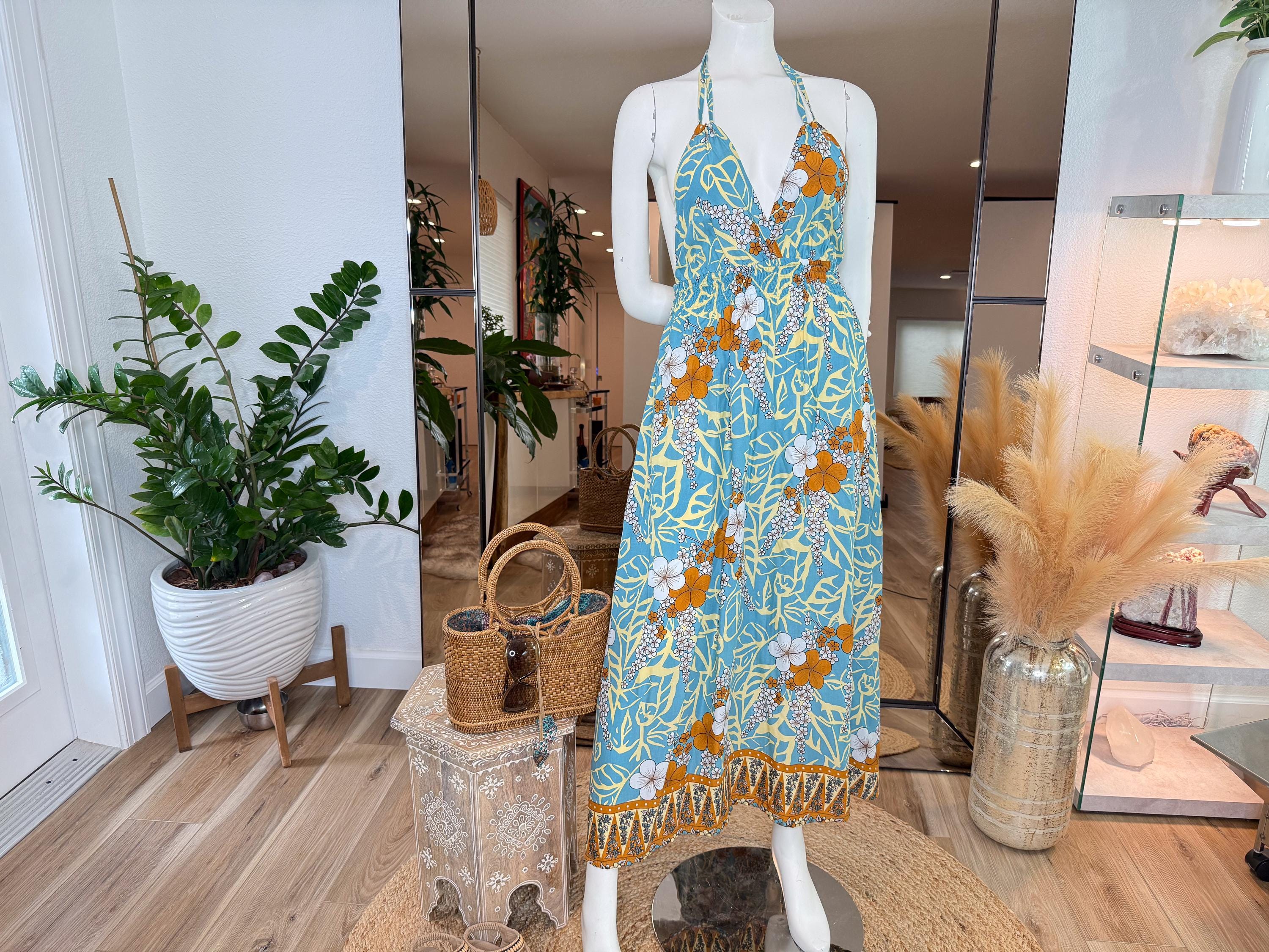 A mannequin wearing a blue and yellow floral print dress stands in a room with various decorative elements, including potted plants and a large mirror.