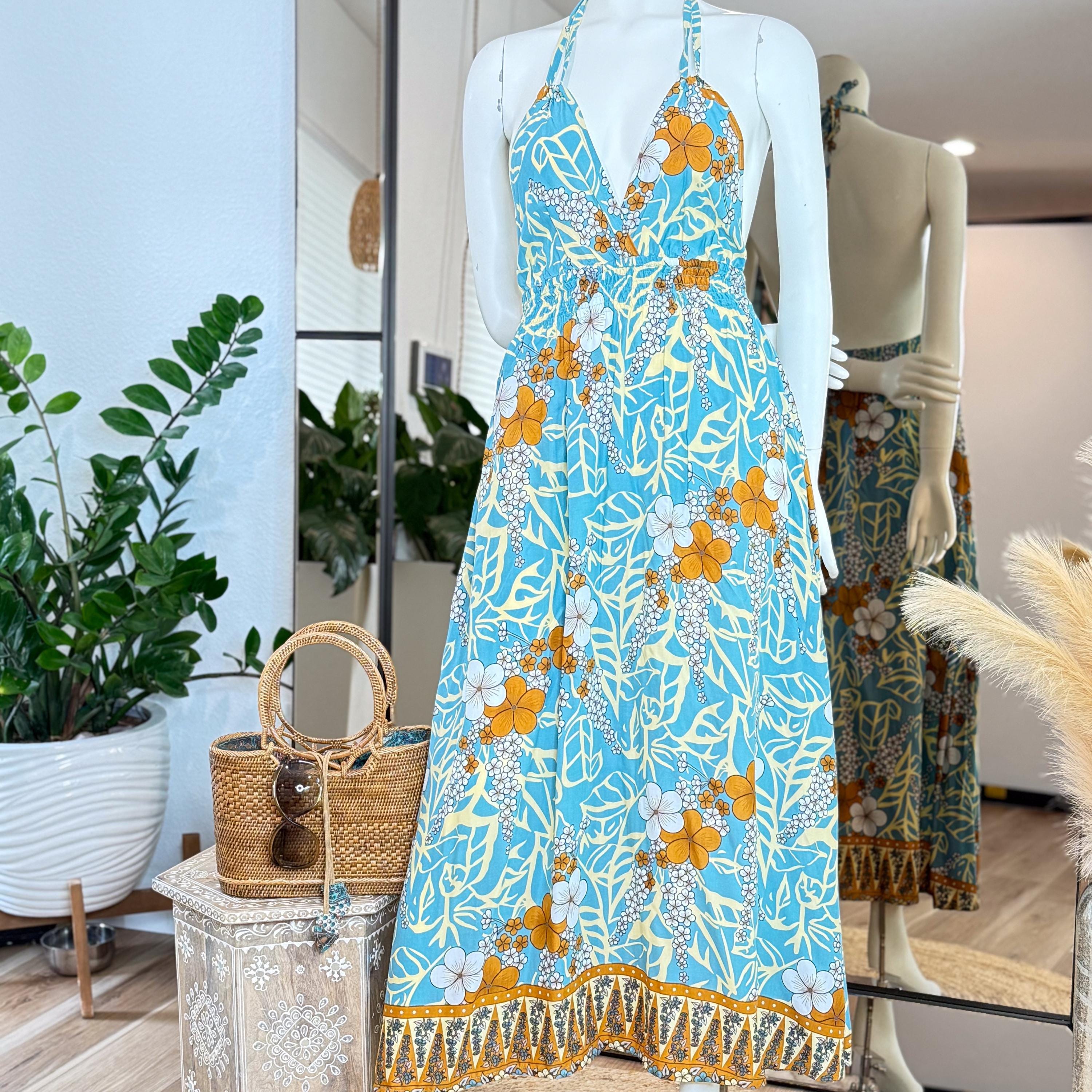 A mannequin wearing a blue and orange floral print dress, with a straw handbag and a potted plant in the background.