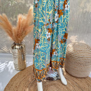 a mannequin wearing a colorful floral print skirt, placed on a woven mat. Next to the mannequin, there is a vase with orange and white flowers, and a woven basket.