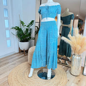 A mannequin wearing a blue off-the-shoulder dress and matching skirt is displayed in a clothing store, with a mirror and potted plants in the background.