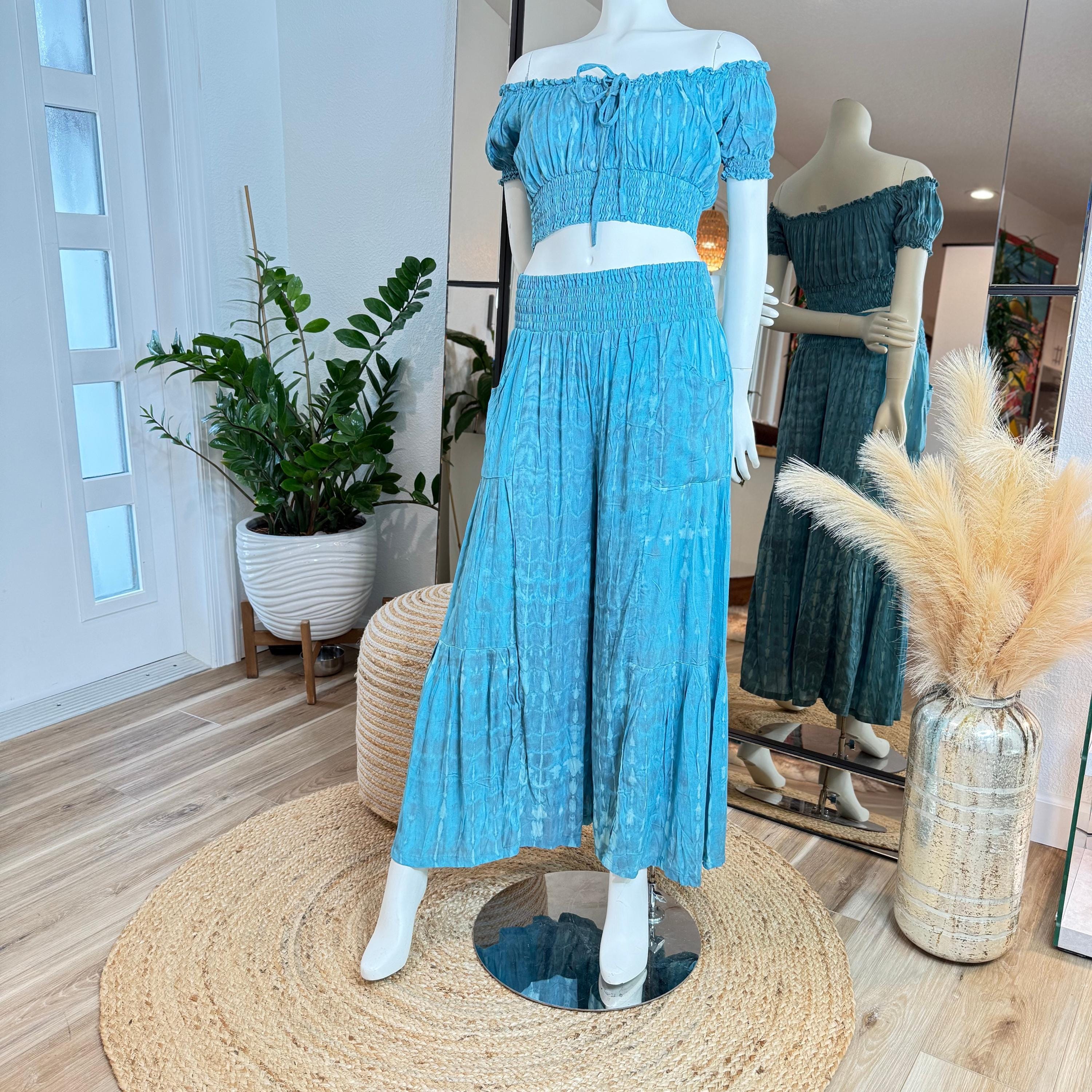 A mannequin wearing a blue off-the-shoulder dress and matching skirt is displayed in a clothing store, with a mirror and potted plants in the background.
