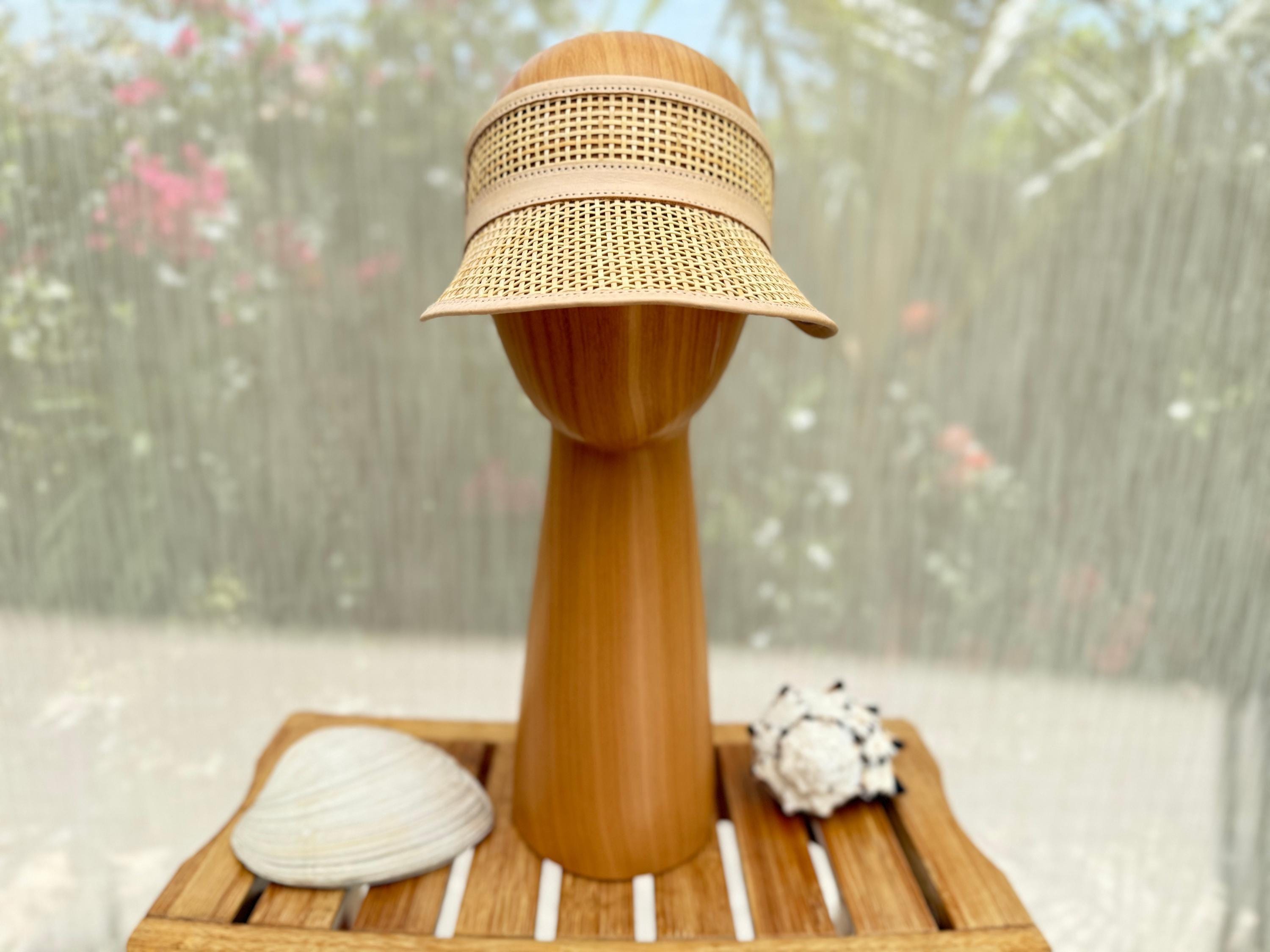 A straw hat with a woven visor is placed on a wooden stand, accompanied by a seashell and a small white object.