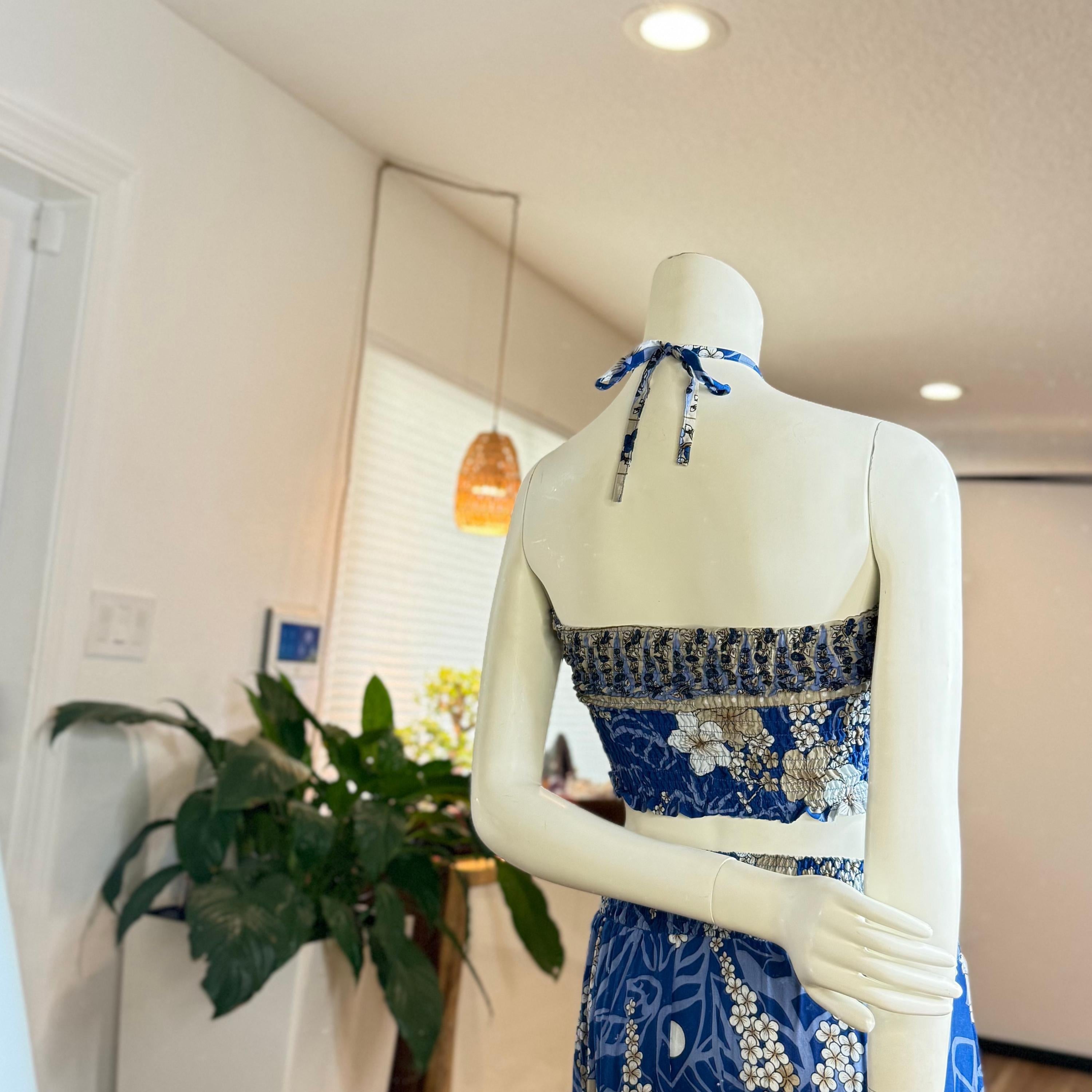 A mannequin wearing a blue and white floral dress stands in a room with a potted plant and a hanging light fixture.