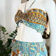 A mannequin wearing a colorful, patterned halter top and skirt, displayed in a retail setting with plants in the background.