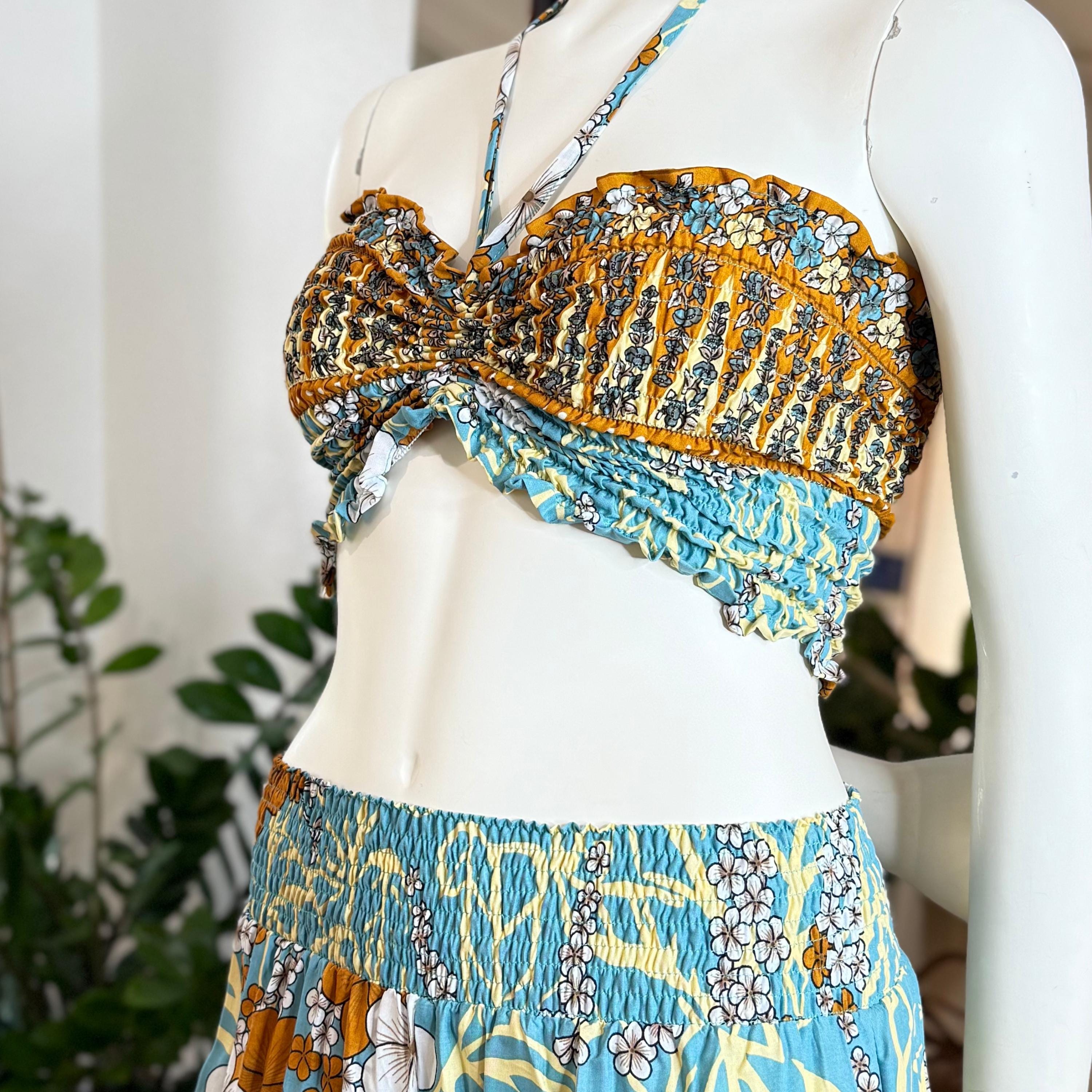 A mannequin wearing a colorful, patterned halter top and skirt, displayed in a retail setting with plants in the background.