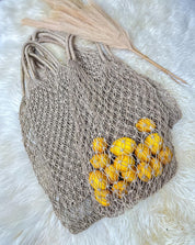 A beige mesh bag filled with bright yellow lemons rests on a white furry surface.