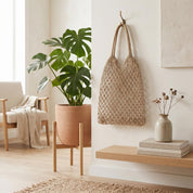 a serene and cozy living space with a large potted monstera plant, a woven bag, a stack of books, and a wooden shelf with a vase of dried flowers.