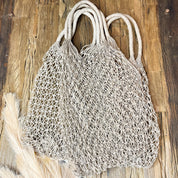 Two white mesh bags with handles are placed on a wooden surface.