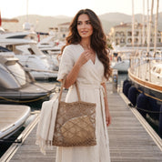 A woman in a white dress stands on a dock, holding a woven bag and wearing a straw hat.