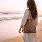 A woman in a white dress stands on a beach, gazing out at the ocean at sunset.