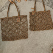 Two woven handbags made of brown, braided material are placed on a textured surface.