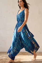 A woman wearing a blue and white tie-dye dress is walking barefoot in front of a plain white wall.