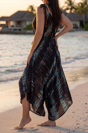 A woman in a colorful dress stands on a beach, facing the ocean.